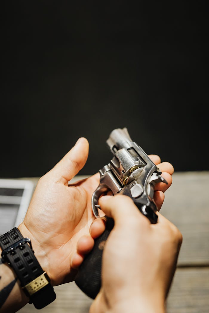 Detailed shot of hands inspecting a silver revolver in a dimly lit setting.